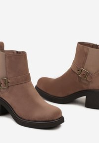 Bottines en suede marron avec un bout rond et un talon moyen. Dotées d'un détail de boucles sur le côté et d'un empiècement contrastant en marron plus clair.