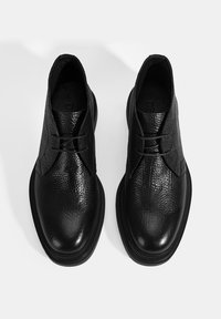 Schwarze Lederschuhe mit strukturiertem Finish, runder Zehenpartie und kontrastierender, glatter Sohle. Verfügen über minimale Schnürung und ein niedriges Knöchel-Design.
