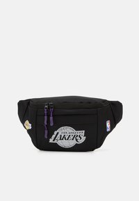 Juodas fanny pack'as su Los Angeles Lakers logotipu, baltu grafikos dizainu, purpurinėmis zipų traukėmis ir NBA logotipo pleistru. Patvari medžiaga.