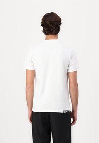 Weißes T-Shirt mit kurzen Ärmeln aus Baumwolle, mit einem runden Halsausschnitt und geradem Schnitt, das ein kleines Markenlabel nahe dem Saum aufweist.