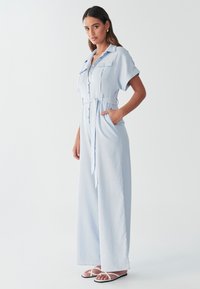 Mono azul claro de tela suave con mangas cortas, cierre frontal con botones, dos bolsillos en el pecho, cintura con cinturón y diseño de pierna ancha.