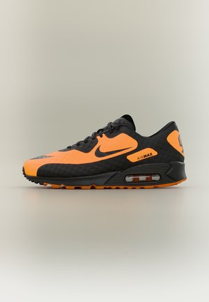 Sneaker Nike Air Max w kolorze czarnym i jaskrawo pomarańczowym z widoczną amortyzacją powietrzną oraz napisem „Air Max” po boku.