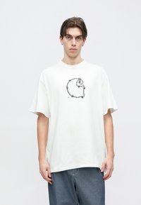 Άσπρο βαμβακερό T-shirt με άνετη εφαρμογή και μαύρο γραφικό με αγκαθωτό σύρμα στο μπροστινό μέρος. Κοντά μανίκια και λαιμόκοψη τύπου crew neck.