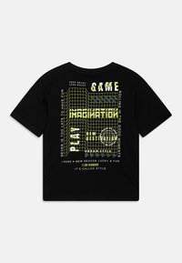 Čierne bavlnené tričko s grafickým dizajnom v neonovo žltej farbe. Text obsahuje "HRA," "PREDSTAVA," a geometrické mriežkové vzory. Krátke rukávy.