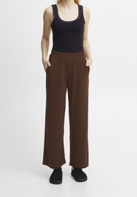 Bruna vidbyxor med elastiskt midjeband och sidofickor, tillsammans med en svart linne och svarta slip-on skor. Slät textur.