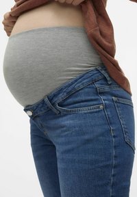 Tamsiai mėlyni džinsai nėščioms moterims su lygiu paviršiumi, turintys tamprų pilvą palaikantį pilkai juostą, užtikrinantys komfortą augančiam pilvui.