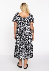 Zwart-wit maxidress met bloemenpatroon, korte rucheslouwen, een ronde hals en een gelaagde zoom. Draag het met zwarte sandalen.