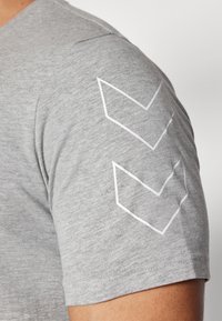 Grå kortærmet t-shirt med en glat tekstur og tre hvide chevrons mønstre på venstre ærme.