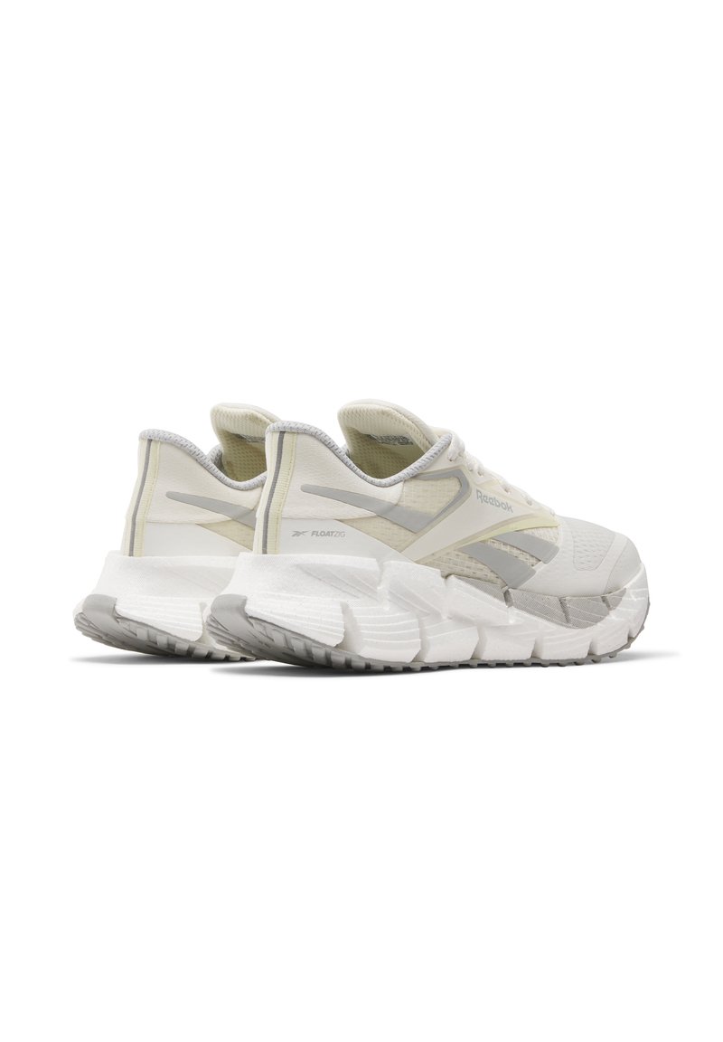 Zapatillas deportivas blancas con una parte superior de malla texturizada, acentos en gris claro y una suela gruesa y segmentada diseñada para amortiguación y soporte.