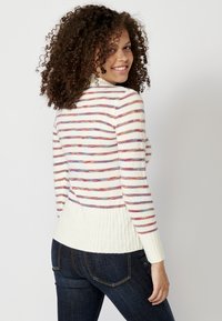 Maglione lavorato a maglia con strisce orizzontali multicolori su uno sfondo bianco, con colletto e orlo a coste. Indossato con jeans in denim scuri.