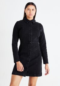 Μαύρο τζιν φόρεμα με μακριά μανίκια, κουμπιά μπροστά και γιακά. Ικανοποιητική εφαρμογή με ορατές ραφές και ελαφρώς φουσκωτό στρίφωμα.