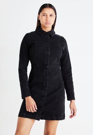 Svart denimklänning med långa ärmar, knäppning fram och krage. Figurformad design med synlig sömnad och en något utställd fåll.