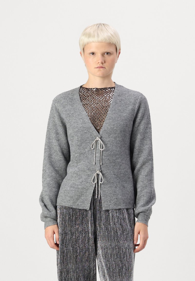 Hallide hallide toegu jääk, millel on pikad varrukad, V-kaelus ja nööriga sulgemine. All pool must võrkkangas top, millel on metallilised niidid.