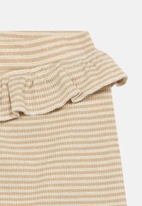 Μπεζ ριγωτός ύφασμα με λευκές ρίγες, που διαθέτει κυματιστό σκισμένο άκρο στην κορυφή. Υφή και ελαφρώς λαμπερή λεπτομέρεια σε όλη την επιφάνεια.