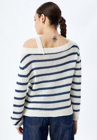 Sweter dzianinowy w kremowo-granatowe paski z dekoltem typu off-shoulder i szerokimi rękawami, charakteryzujący się teksturowaną dzianiną i ryżowym wykończeniem.