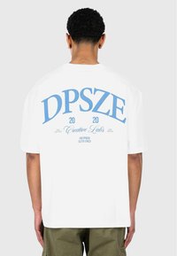 Hvid bomulds t-shirt med stor blå trykt tekst på ryggen, med "DPSZE," "2020," og "Creative Labs," samt yderligere mindre tekst.