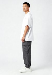 Witte oversized t-shirt, grijze cargobroek met meerdere zakken en witte sneakers. De stof lijkt glad en heeft een relaxte pasvorm.