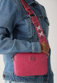 Borsa crossbody in pelle rosa con una texture liscia, caratterizzata da un patch con logo, una tracolla staccabile con dettagli e una forma rettangolare.