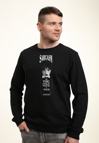 Muž v černé mikině s grafikou dívky s copy a textem "Sarkasmus je jediný přítel, kterého potřebuji ve středu."