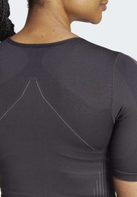 Cămașă athletică neagră cu mâneci scurte, dintr-un material texturat și cu un design elegant. Prezintă cusături reflectorizante subtile și linii ergonomice.