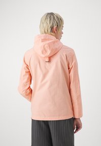 Jachetă cu capușon de culoare piersiciu deschis, cu mâneci lungi, ajustabilă cu un sistem cu toggle pe glugă și o textură netedă, asortată cu pantaloni cu dungi. 