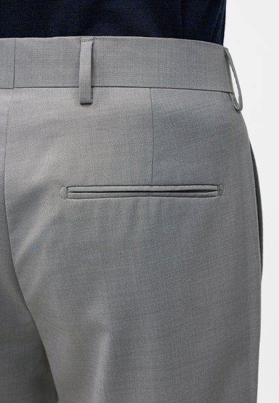 Κοντινή λήψη γκρι παντελονιών προσαρμοσμένης ραφής με έμφαση στην πίσω τσέπη και τις λεπτομέρειες του θηλύκου της ζώνης πάνω σε σκούρο τοπ.