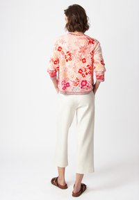 Floral-patterned lightweight sweater in pink and red hues, with long sleeves and contrasting textured cuffs, paired with cream tapered pants.