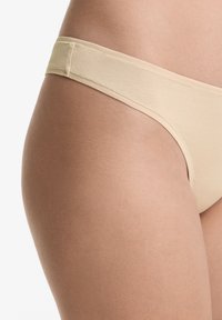 Beige katoenen stringondergoed met een zachte, gladde textuur en een minimalistische tailleband, met een eenvoudig ontwerp en naadloze randen.