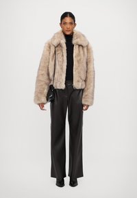 Chaqueta de piel sintética en beige claro con una textura suave, cierre de cremallera y cuello sobredimensionado, combinada con pantalones de cuero negros de cintura alta.