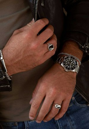 Silver watch with black face, stainless steel bracelet. Silver ring with geometric design. Textured leather jacket. Rough skin texture.