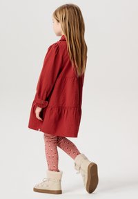 Rotes, leichtes Langarmkleid mit gestuftem Rock, kombiniert mit pinkfarbenen gemusterten Leggings und beigen, mit Fell gefütterten Knöchelstiefeln.
