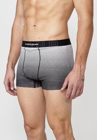Schwarz-weiße gestreifte Boxershorts mit einem schwarzen elastischen Bund, der mit "KOROSHI" beschriftet ist. Glatte Textur, körperbetonter Schnitt und knielange Ausführung.
