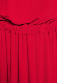 Robe rouge avec une taille froncée et un tissu fluide, présentant une texture lisse et une couleur vibrante et uniforme sur toute la surface.