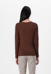 Top lung cu mânecă lungă de culoare maro, fabricat dintr-un material moale, având un decolteu rotund și o croială slim, asortat cu pantaloni cu un model în carouri.