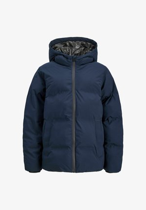 Tumesinine pufferjakk kapuutsiga, lukkudega ja soonikutega varrukate ääres, kantud tumeda kampsuni ja hele pluusi peale. Kandmisel lahtised teksapüksid.