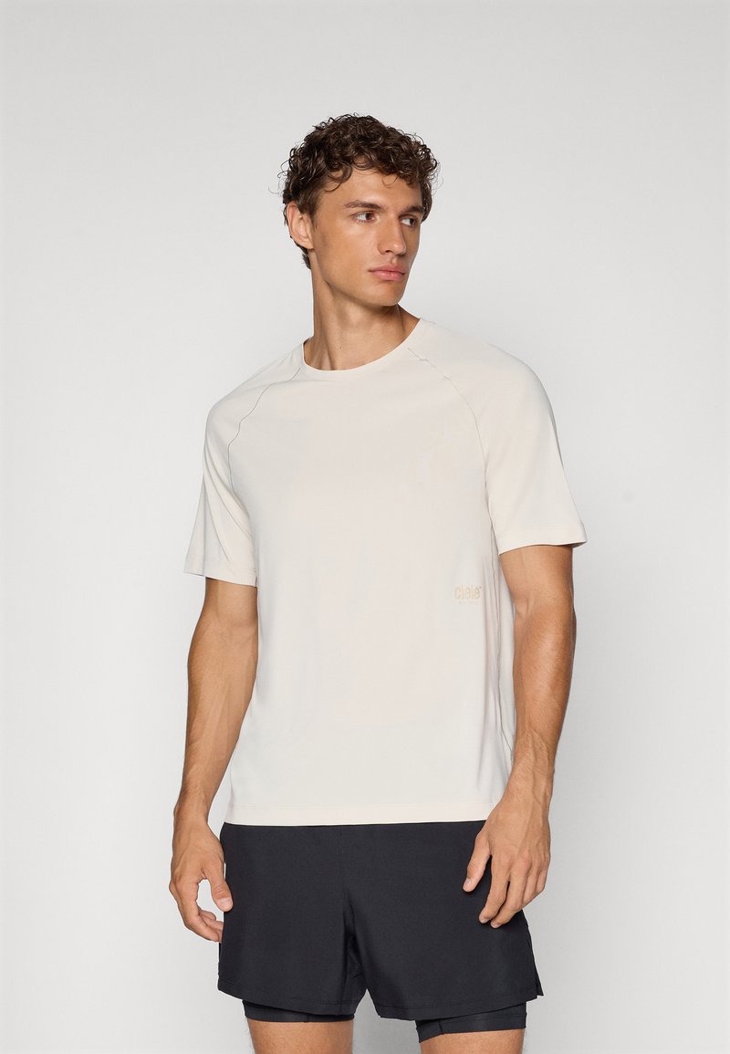 Ljusbeige kortärmad t-shirt med rund hals och raglanärmar. Har minimal varumärkeslogga i en ljusare nyans. Mjuk tygtextur.