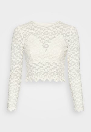 Biały koronkowy top z długim rękawem, krótkim krojem, kwiatowym wzorem i falistymi brzegami, z dekoltem w kształcie serca oraz przezroczystymi rękawami.