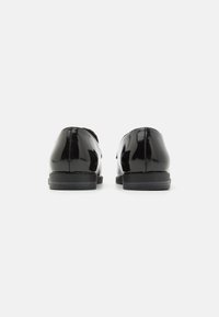 Chaussures en cuir verni noir avec une finition lisse et brillante, présentant un design discret et une semelle plate noire. Pas de matériel ou de décorations visibles.