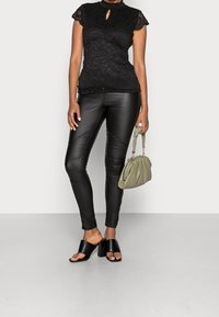 Sort blonderet top med nøglehul detalje, parret med tætsiddende sorte læderbukser, sorte blokhælede sandaler og en grøn taske.