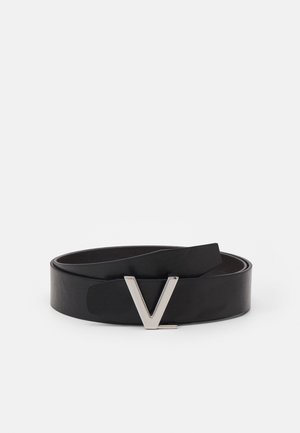 Ceinture en cuir noir enroulée avec une boucle métallique argentée en forme de V sur un fond blanc uni.