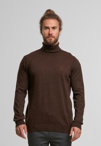 Brauner Rollkragenpullover aus einem weichen Strickmaterial. Verfügt über enganliegende lange Ärmel und gerippte Bündchen, mit dezentem Logo-Detail auf der Brust.