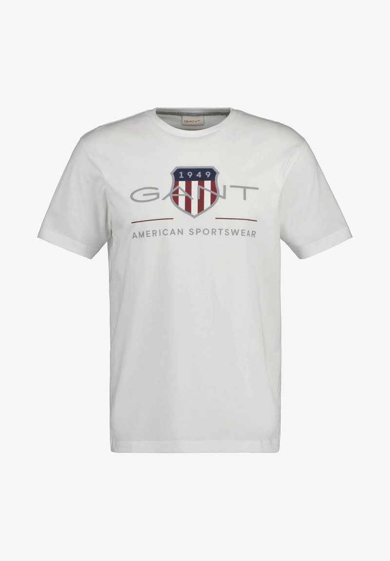 T-shirt en coton blanc avec un logo écusson bleu et rouge, "GANT" imprimé au-dessus, avec "1949" et le texte "AMERICAN SPORTSWEAR" en dessous.