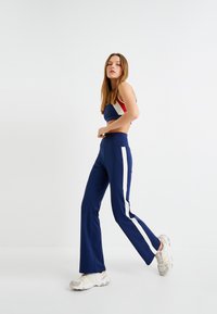Marineblauw sportief crop top met witte en rode accenten, gecombineerd met bijpassende flared broeken met witte zijkanten en een gladde textuur.