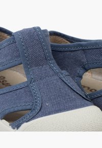 Le scarpe di tela blu presentano una tomaia strutturata con tessuto testurizzato, fasce elastiche e una suola in gomma bianca con una finitura a motivo.