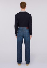 Camisa de manga larga azul oscuro con cuello redondo, combinada con unos vaqueros de denim azul de corte holgado que cuentan con una etiqueta de cuero y bolsillos traseros estándar.