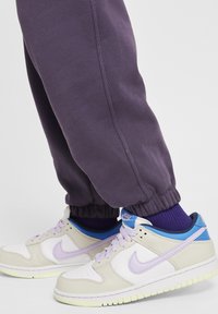 Nike tornacipő tejszínből és világoslilából kék árnyalatokkal és sárga talppal, sötétlila melegítőnadrággal, amelynek elasztikus szegélyei vannak.