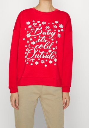 Osoba nosząca czerwoną bluzę z białymi śnieżynkami i frazą „Baby it’s cold outside” pisaną ozdobnym pismem.