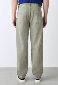 Light gray jeans with a loose fit, two back pockets, and a plain waistband. Paired with black and white sneakers.