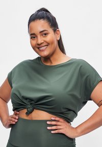 Green, ribbed short-sleeve cropped top with a front knot detail, paired with matching high-waisted leggings. Smooth fabric texture.