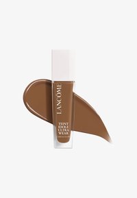 Lancôme Teint Idole Ultra Wear foundation i en klar flaske med hvit hette. Rikt brunt væskeprøve ved siden av, glatt tekstur, kremet konsistens.